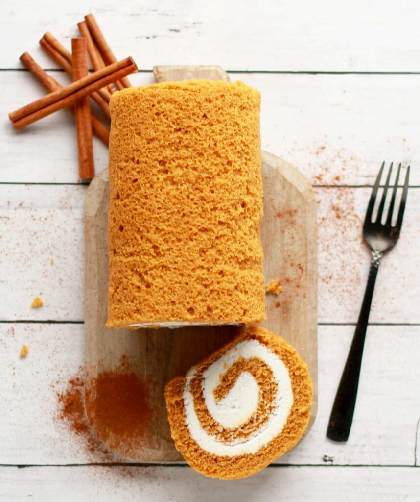Pumpkin Spice Cake Roll with Buttercream Frosting on a wooden board with cinnamon powder and cinnamon sticks.