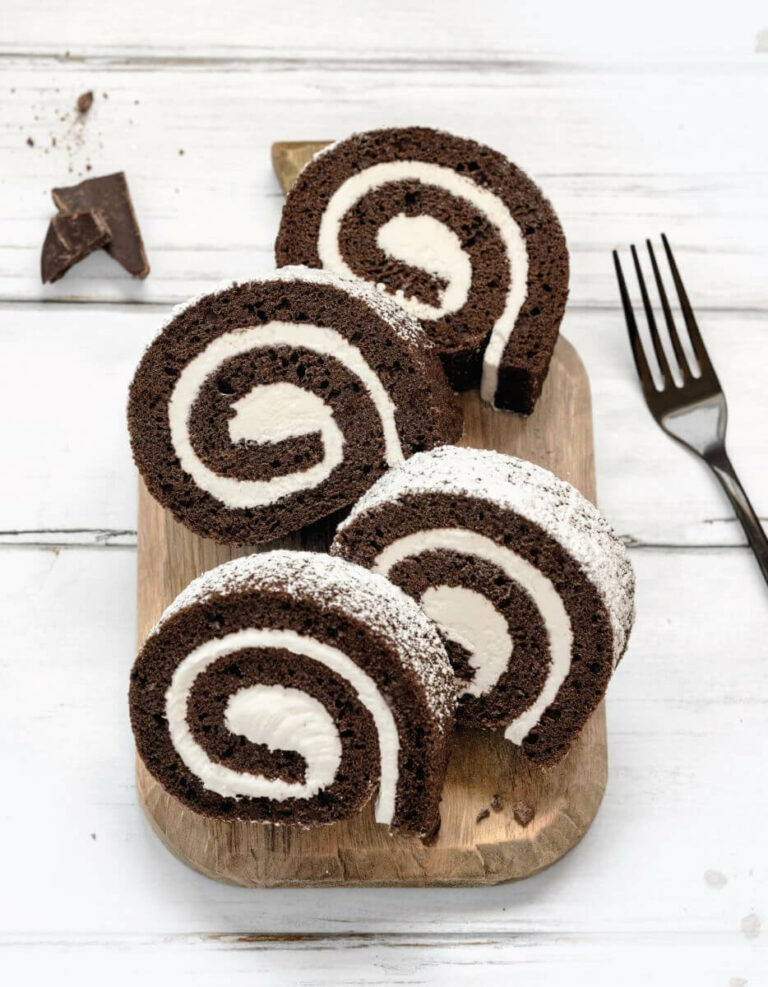 Slices of River Bend's Chocolate Cake Roll on a wooden cutting board which is on a white wood background.