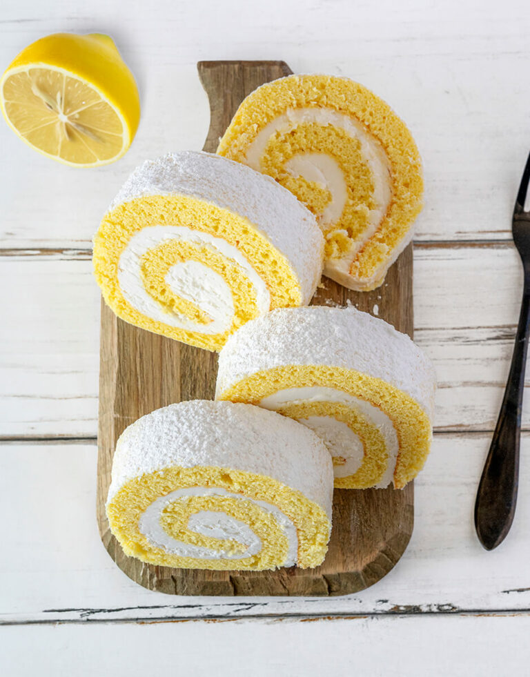 Slices of Lemon Cake Roll on cutting board with half a lemon on white wooden background