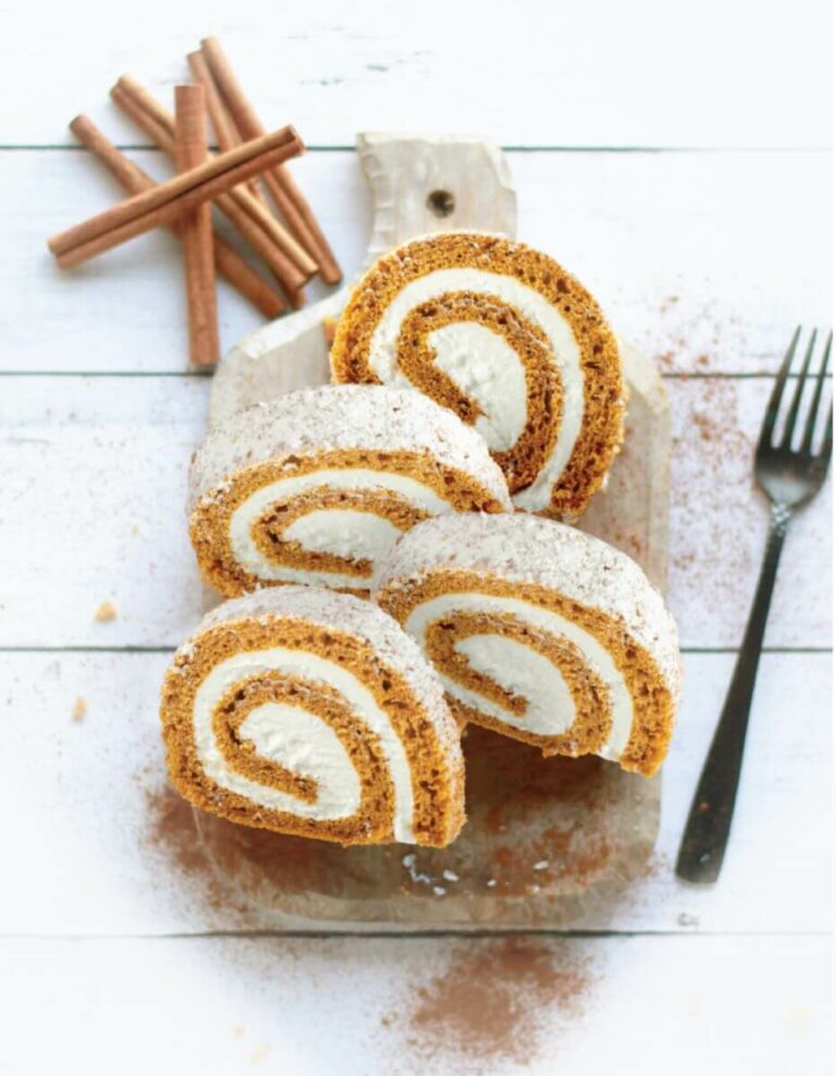Slices of Pumpkin Spice Cake Roll on cutting board with cinnamon sticks on white wooden background