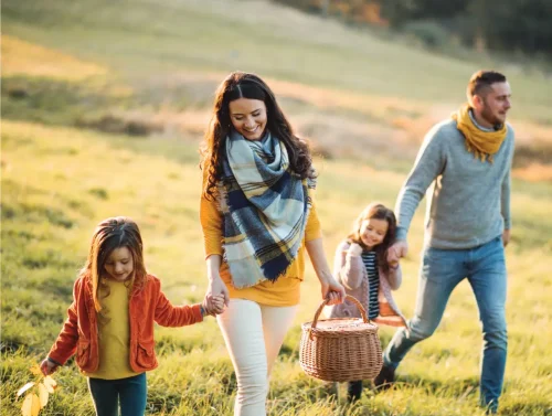River Bend Mom and Dad with two adorable girls walking through a grassy field to have a picnic on a crisp fall day.