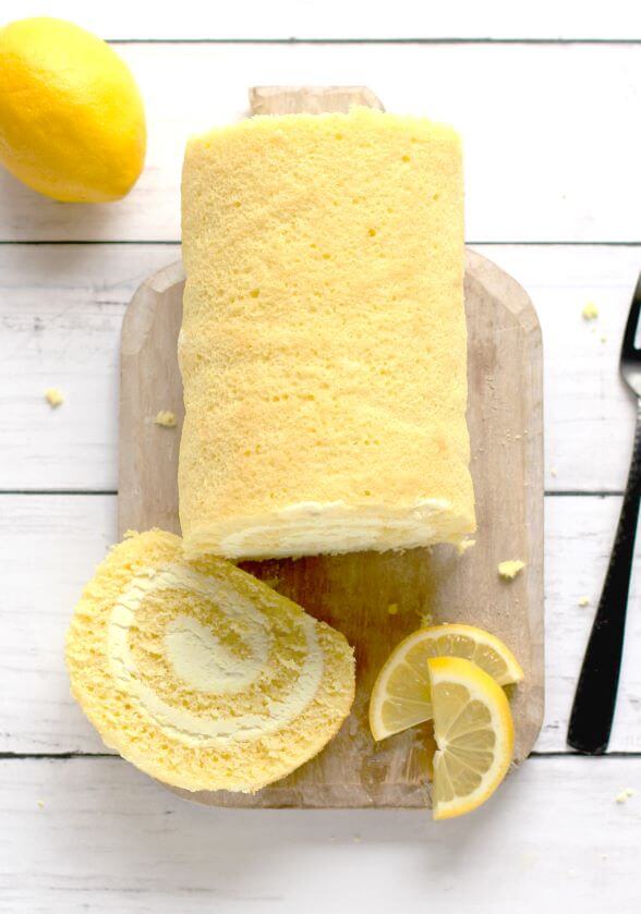 lemon cake roll with lemon and lemon slices on a cutting board next to a fork