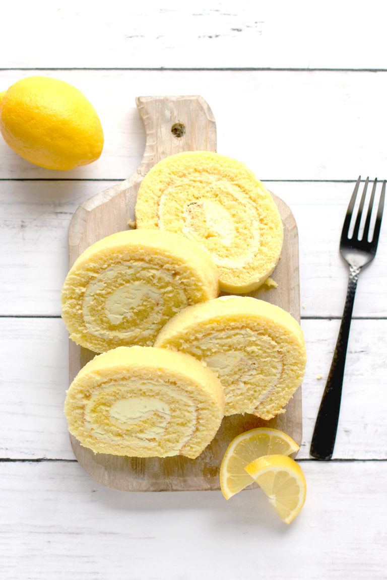 Slices of Lemon Cake Roll with Lemon Flavored Buttercream Frosting arranged on a wooden board with fresh lemon slices.