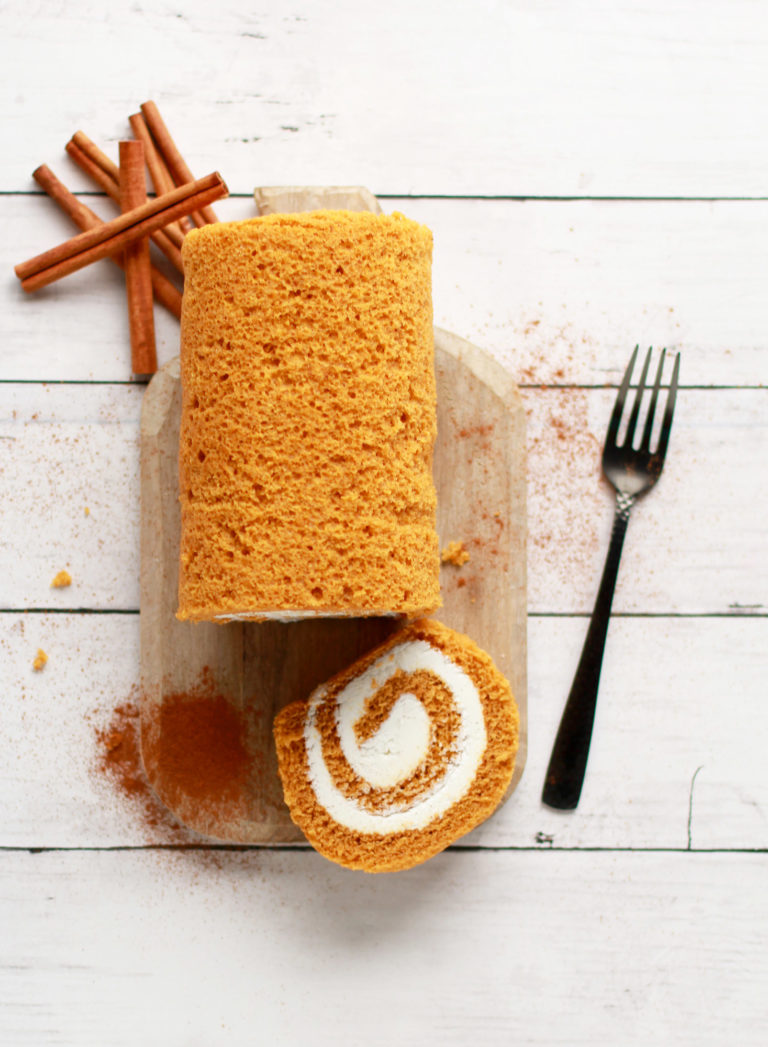 Pumpkin Spice Cake Roll with Buttercream Frosting on a wooden board with cinnamon powder and cinnamon sticks.